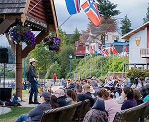 Musician performing on an outdoor gazebo stage for a seated crowd at the June Tunes community concert