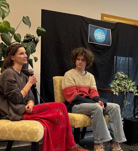 West Sound Academy Lead with Confidence A host holding a microphone speaks beside a seated student in front of a Wednesday Afternoon Show backdrop
