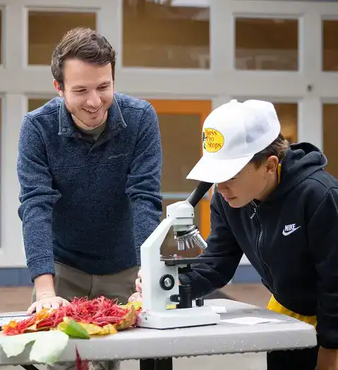 West Sound Academy Think Boldly Teacher guiding a student examining a specimen through a microscope during a hands-on science lesson
