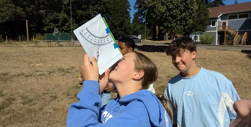 West Sound Academy Upper School Upper School student using a protractor to measure angles outdoors, with classmates nearby