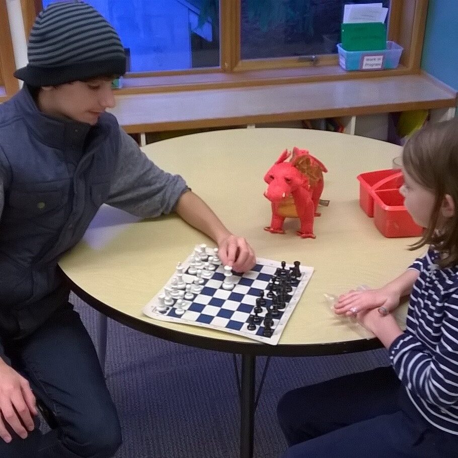 Game Club member teaches chess to a young student at a local school